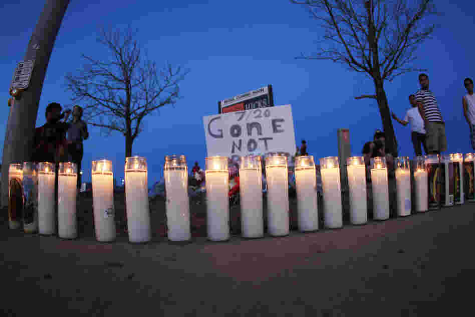 As night falls Friday, candles sit iluminated along the sidewalk in front of a makeshift memorial for the victims. After the shooting, 24-year-old suspect James Holmes was arrested.