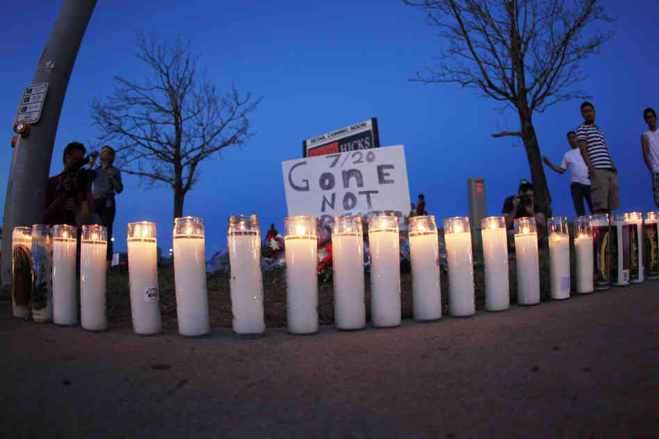 As night falls Friday, candles sit iluminated along the sidewalk in front of a makeshift memorial for the victims. After the shooting, 24-year-old suspect James Holmes was arrested.
