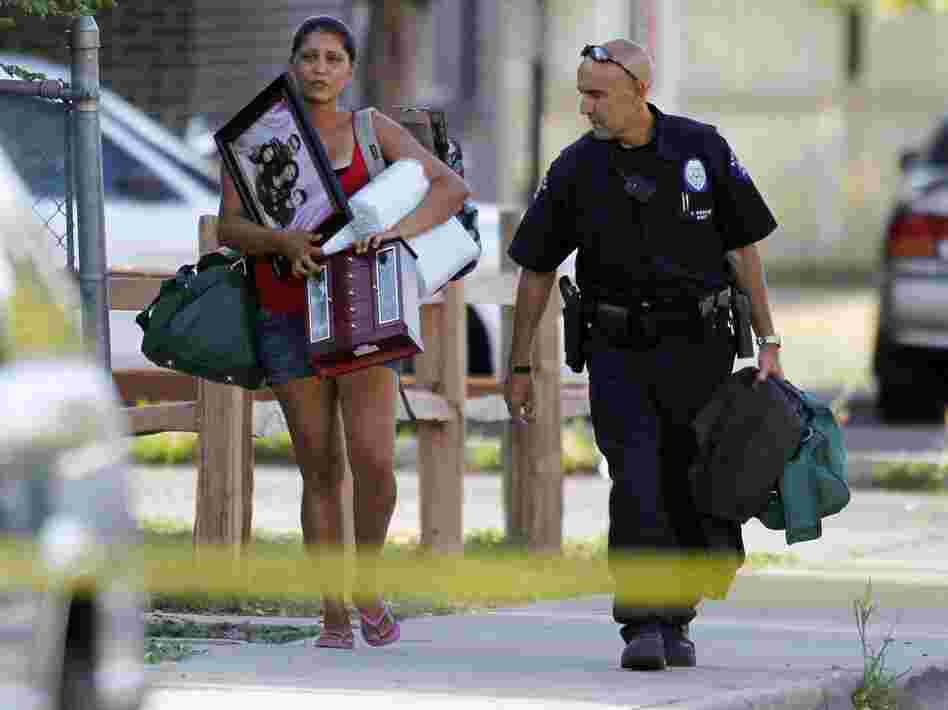 An Aurora police officer assists a woman carrying her belongings from her home near the apartment of alleged gunman James Holmes. Bomb technicians are working to defuse his booby-trapped apartment.