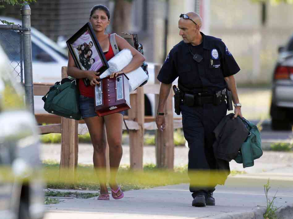An Aurora police officer assists a woman carrying her belongings from her home near the apartment of alleged gunman James Holmes. Bomb technicians are working to defuse his booby-trapped apartment.