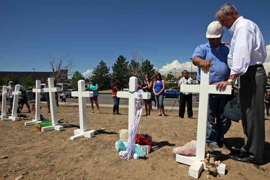 Aurora, Colo., Mayor Steve Hogan (right) says a prayer with Greg Zanis, from Aurora, Ill., as Zanis places crosses for the victims across the street from the movie theater where the mass shooting took place.