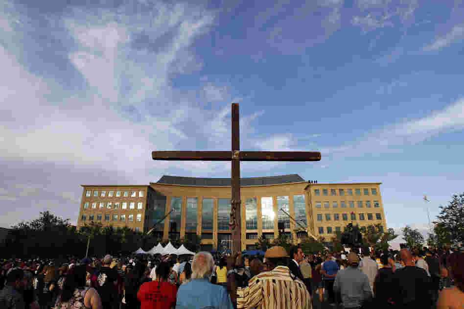 A cross stands among people gathered for the vigil at the Aurora Municipal Center Sunday.