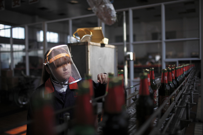 A worker inspects labels on beer bottles as they move down the production line at a brewery in Nanjie village, Henan province, China, November 2009. Nanjie is a collective village run along Maoist lines. Residents have socialist benefits like free education and health care, but there is no private property.