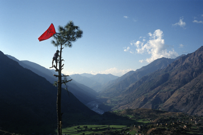 Nabin Pun, a Maoist rebel soldier of the People's Liberation Army, raises the communist flag from a tree above the village of Rukumkot, Nepal, February 2005.