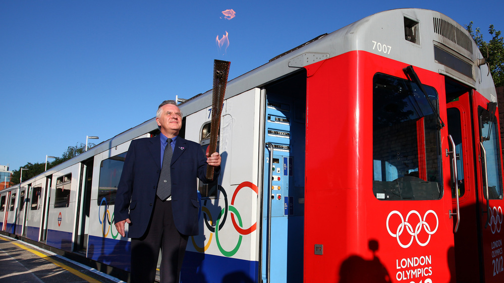 London Underground employee John Light (!) carries the Olympic torch onto a train at Wimbledon Station.