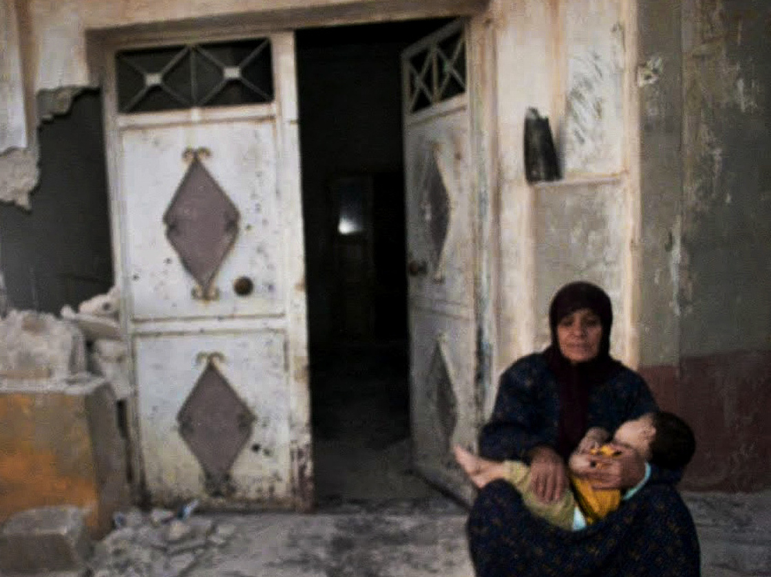 In this image provided by the Syrian opposition's Shaam News Network, a woman holds a child in front of their destroyed home in Tremseh, Syria, on July 14. The authenticity, content, location and date have not been independently verified.