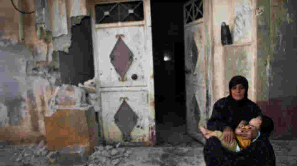 In this image provided by the Syrian opposition's Shaam News Network, a woman holds a child in front of their destroyed home in Tremseh, Syria, on July 14. The authenticity, content, location and date have not been independently verified.