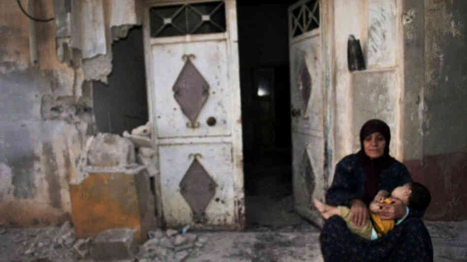 In this image provided by the Syrian opposition's Shaam News Network, a woman holds a child in front of their destroyed home in Tremseh, Syria, on July 14. The authenticity, content, location and date have not been independently verified.