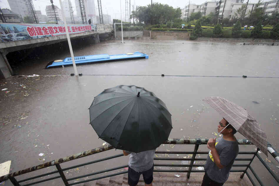 Residents look at a submerged bus on a flooded street in the Chinese city of Tianjin on Thursday. Beijing and neighboring areas have experienced the worst rainstorms in six decades. At least 77 people were killed, Chinese authorities said Thursday.