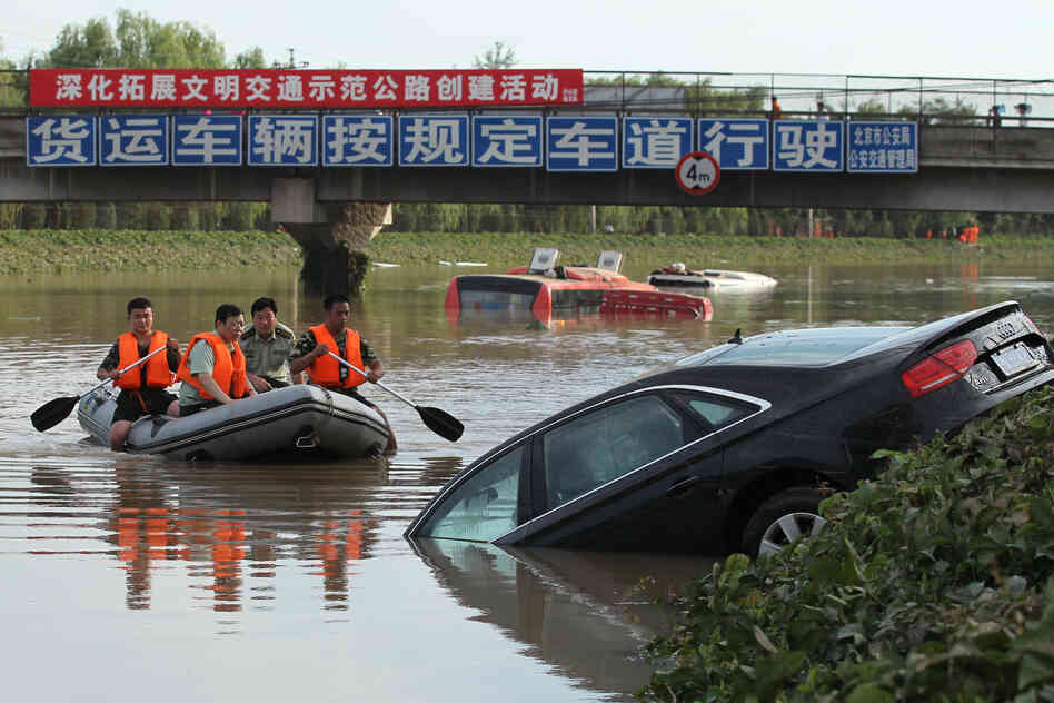 A rescue boat approaches a partially submerged car on a highway in the Fangshan District of Beijing.