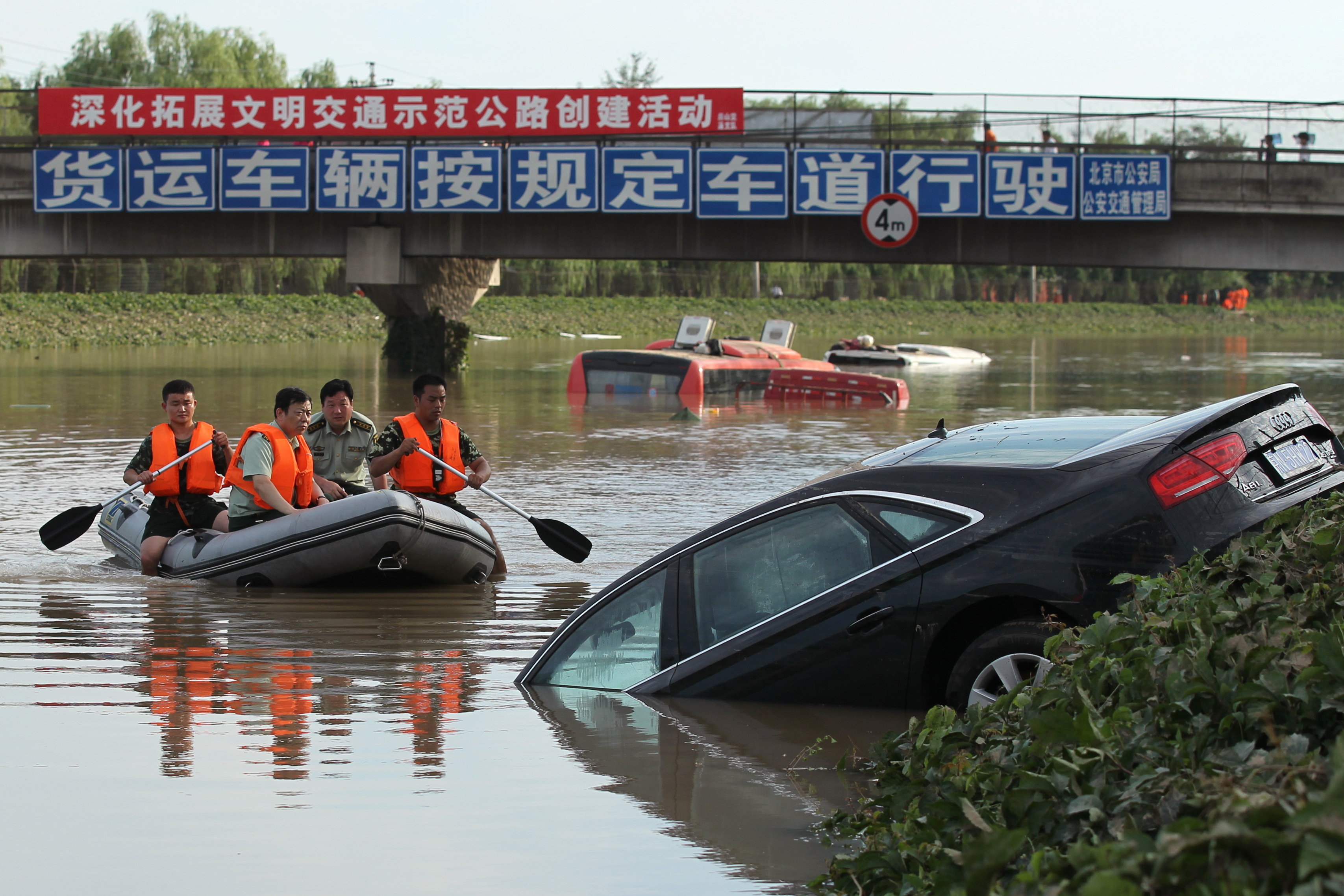 A rescue boat approaches a partially submerged car on a highway in the Fangshan District of Beijing.
