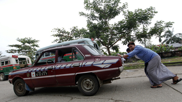 An old taxi is pushed toward a vehicle license office to be exchanged for an import permit in Yangon, Myanmar. As many Burmese citizens take cars as an investment, many imports are sold and resold with a higher markup.