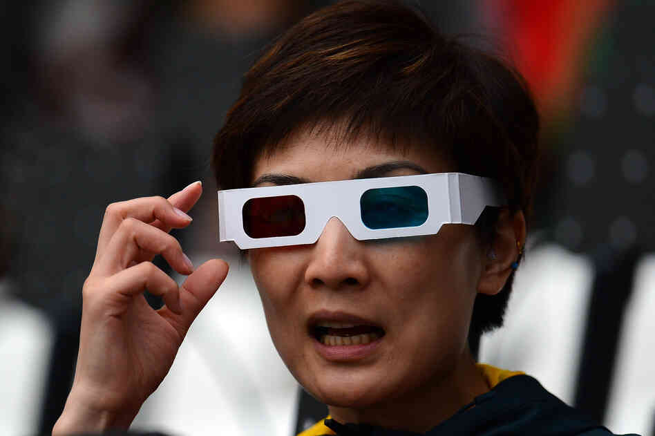 A fan wearing 3-D glasses watches the ceremony.