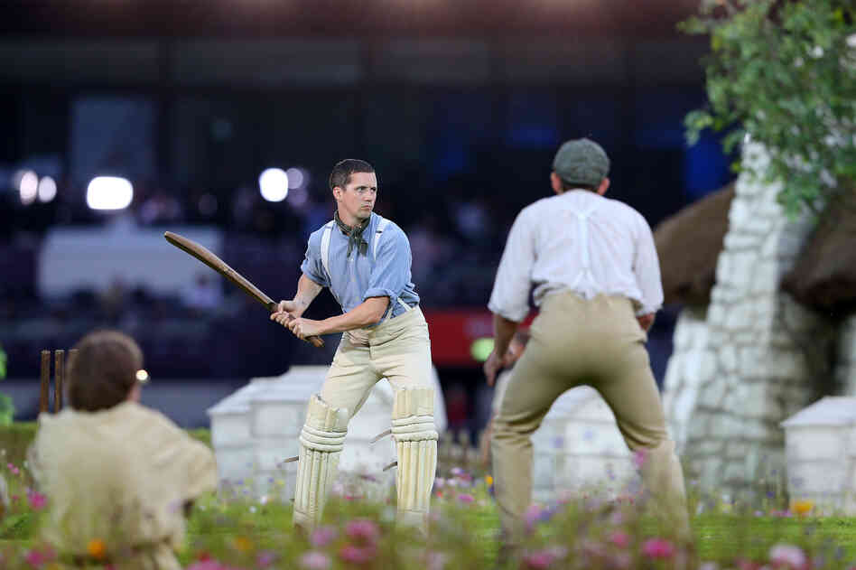 Performers depict a view of the English countryside by playing a game of cricket.