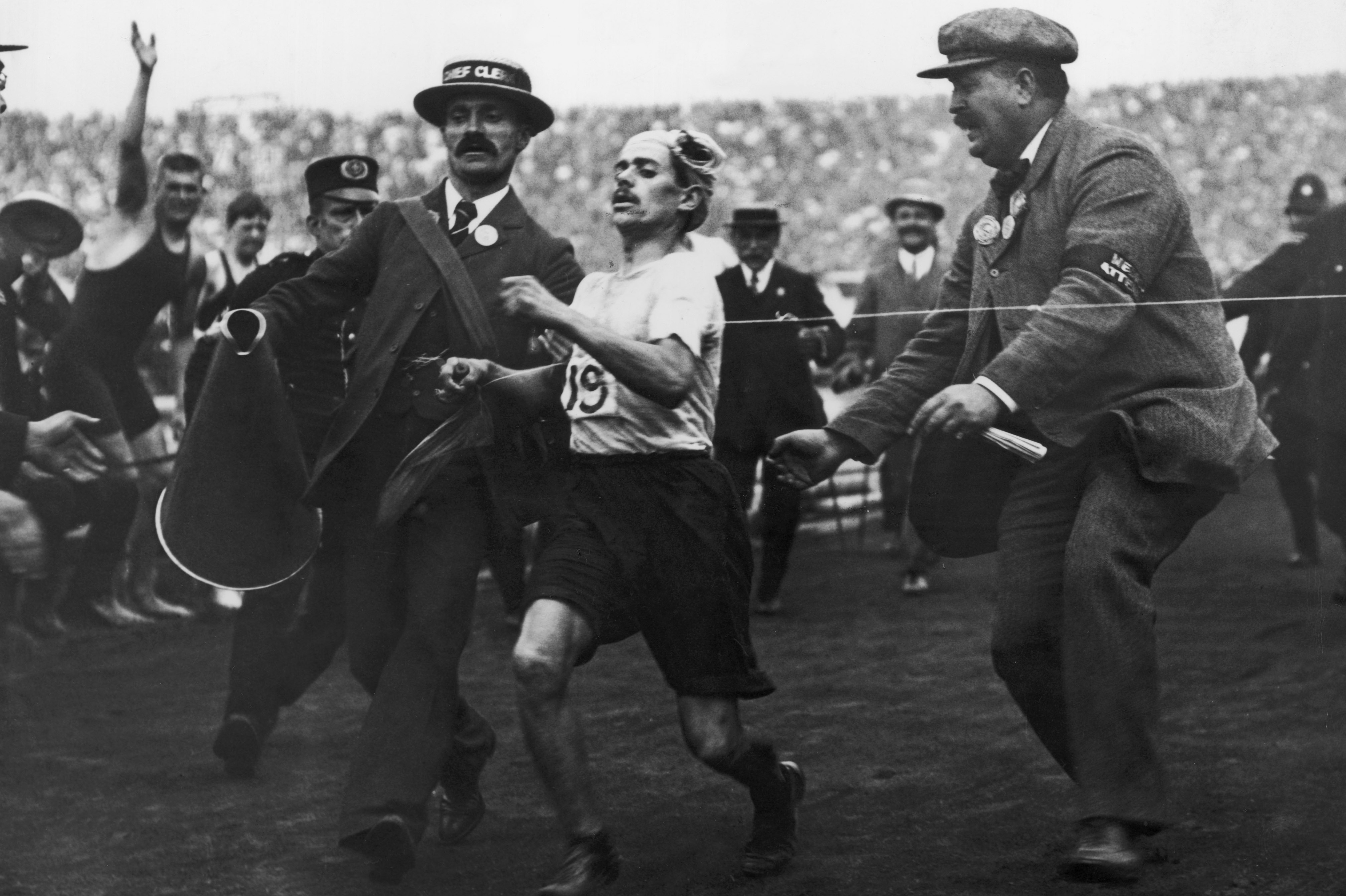 Dorando Pietri of Italy, on the verge of collapse, is helped across the finish line in the marathon. He was subsequently disqualified and the title was given to John Hayes of the United States.