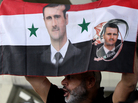 A Syrian man holds a national flag bearing pictures of President Bashar Assad during a pro-regime protest to condemn a deadly attack in the central Midan district of Damascus on April 27. A Syrian man holds a national flag bearing pictures of President Bashar Assad during a pro-regime protest to condemn a deadly attack in the central Midan district of Damascus on April 27.