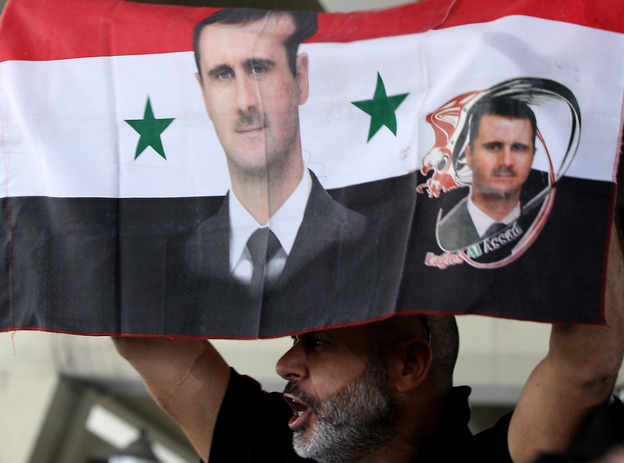 A Syrian man holds a national flag bearing pictures of President Bashar Assad during a pro-regime protest to condemn a deadly attack in the central Midan district of Damascus on April 27.