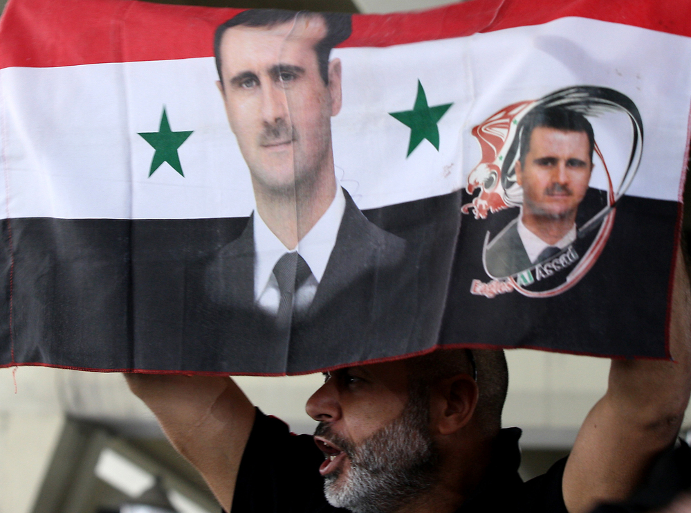 A Syrian man holds a national flag bearing pictures of President Bashar Assad during a pro-regime protest to condemn a deadly attack in the central Midan district of Damascus on April 27.