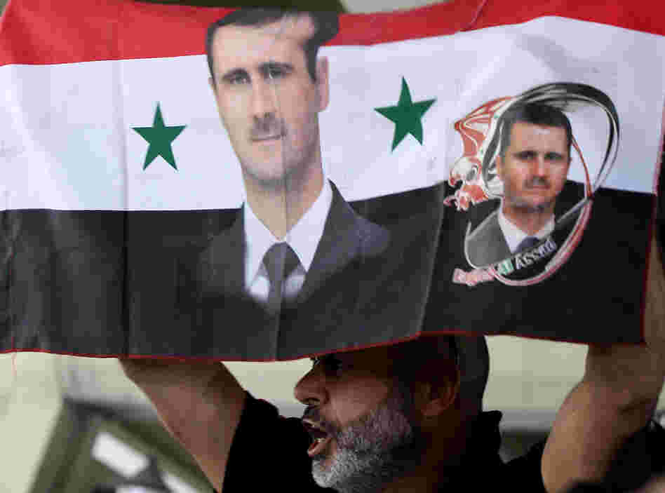 A Syrian man holds a national flag bearing pictures of President Bashar Assad during a pro-regime protest to condemn a deadly attack in the central Midan district of Damascus on April 27.
