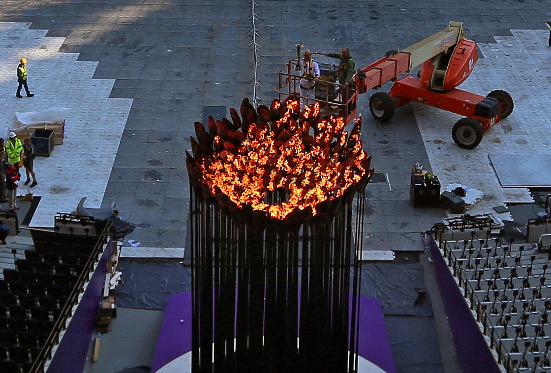 In a mostly empty Olympic Stadium, Austin Playfoot lights the Olympic cauldron Monday morning. The cauldron was extinguished Sunday night, so it could be moved to one end of the stadium. Click the enlargement to see a close-up view.