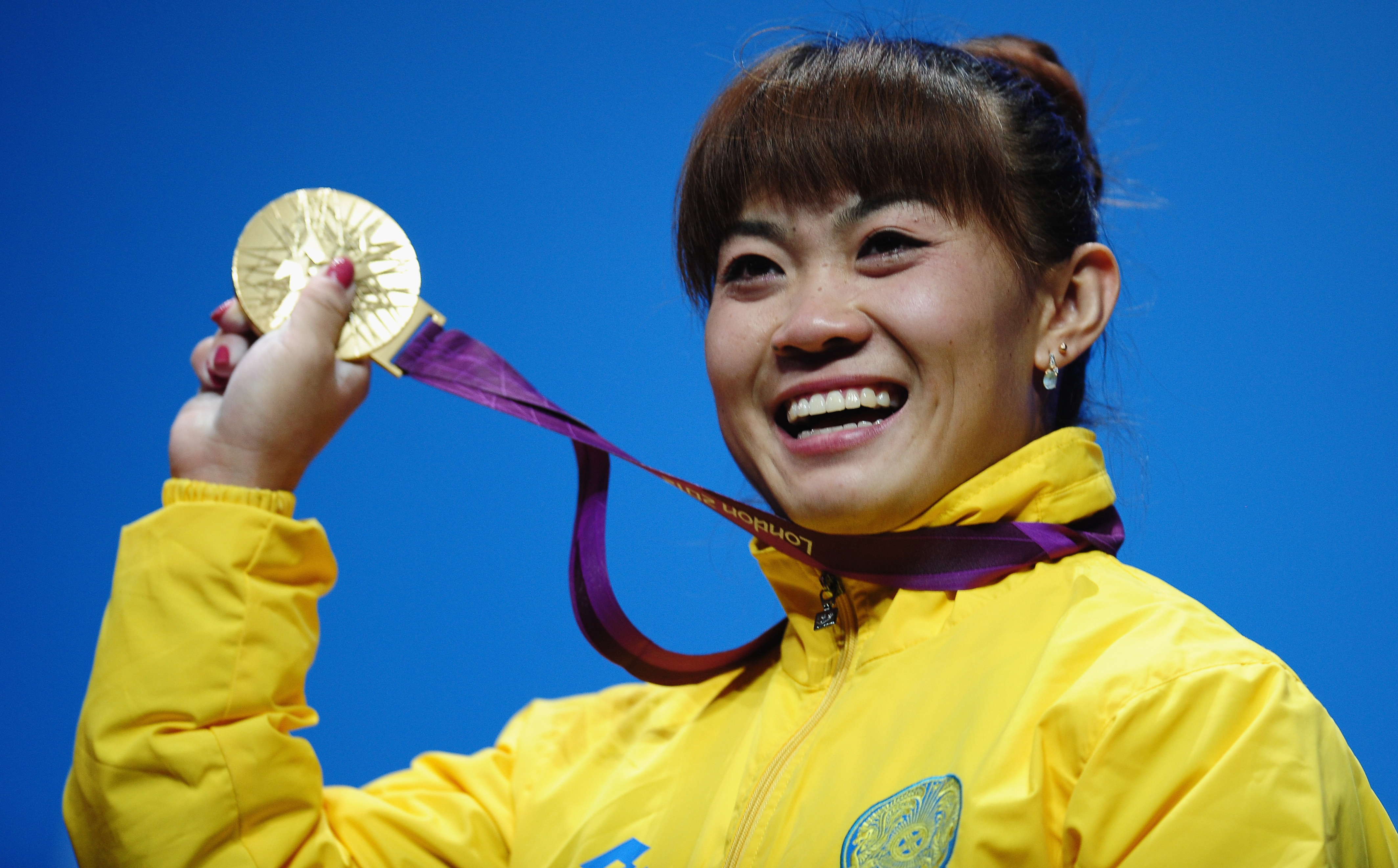 <strong>Plenty To Smile About:</strong> Weightlifter Maiya Maneza of Kazakhstan celebrates on the podium with her new 400-gram gold medal, matching the feat of her compatriot Zulfiya Chinshanlo. The Kazakh Olympians will each receive a $250,000 bonus.