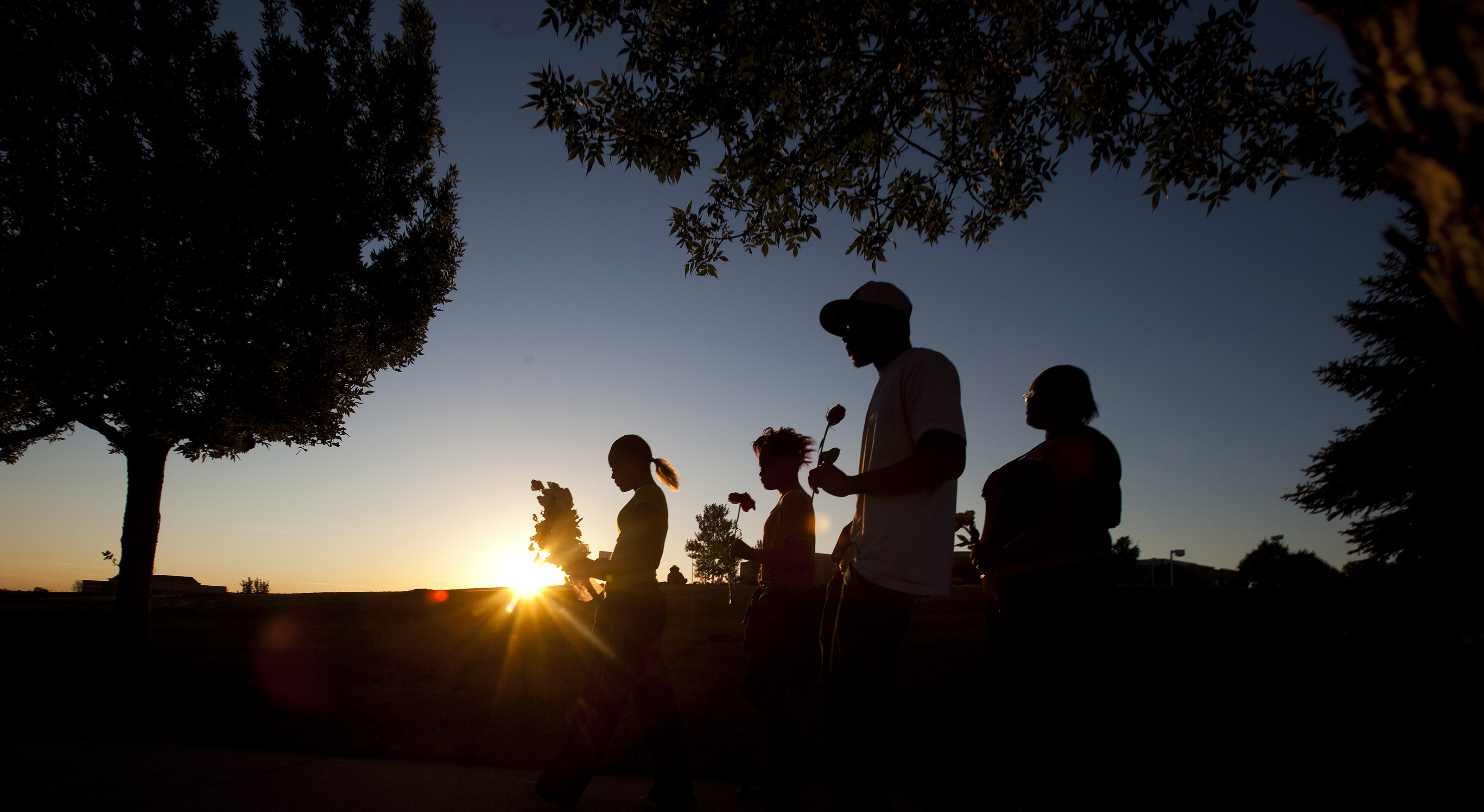 From left, Tylecia Amos, 14, Shatyra Amos, 15, Michael Walker, 17, and Mykia Walker, 16, carry flowers to a makeshift memorial across the street from the Century Theater parking lot on July 21. Walker was a classmate of AJ Boik, who was killed in the shooting.