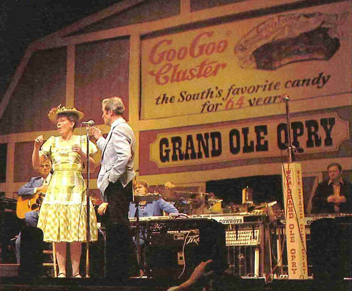 Minnie Pearl and Roy Acuff perform in front of a Goo Goo Cluster advertisement at the Grand Ole Opry, circa 1976. Coincidentally, Pearl's 100th birthday is also in October.