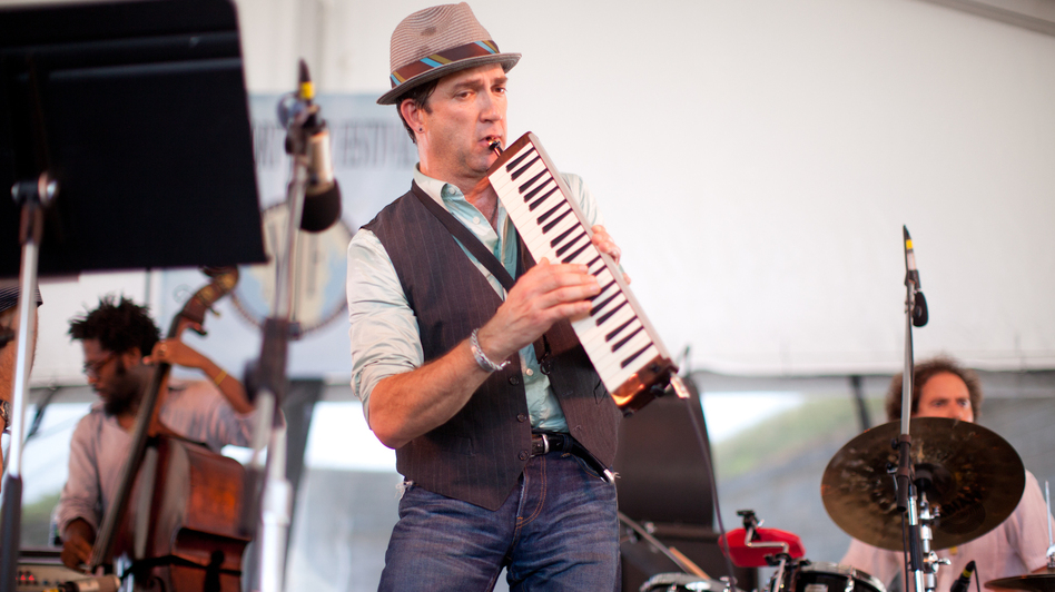 Saxophonist Peter Apfelbaum (center) plays the melodica at the 2012 Newport Jazz Festival, accompanied by Yunior Terry (left) on bass and Dafnis Prieto (right) on drums.