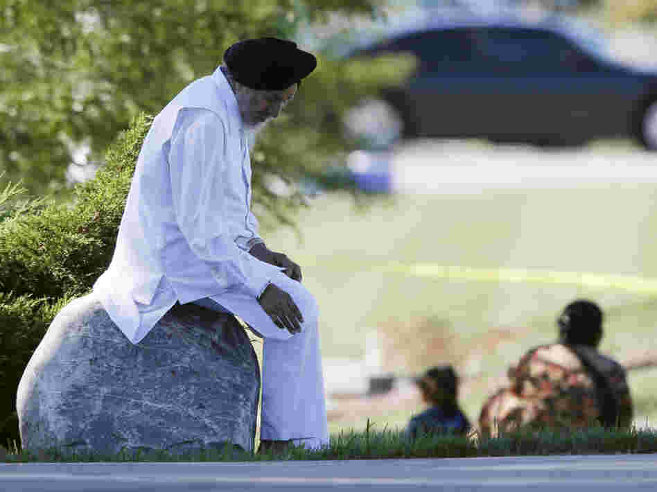 A man sits on a rock as police investigate.