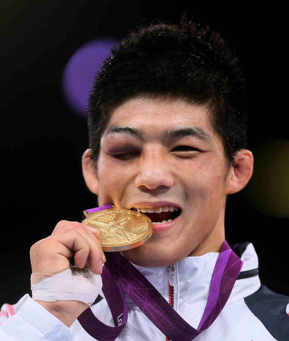 South Korea's Kim Hyeonwoo, winner of the gold medal in the 66-kilogram Greco-Roman Wrestling event, bites his medal as he poses on the podium. He won the final despite a badly swollen eye.