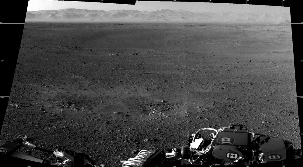 A photograph taken by NASA's Curiosity Rover on Mars. The rim of Gale Crater can be seen in the distance beyond the pebbly ground.