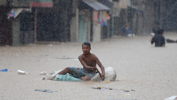 A man paddled an improvised raft along a flooded street in suburban Manila earlier today.