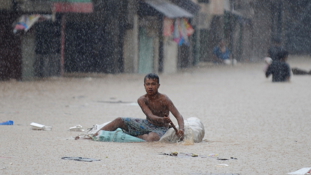 A man paddled an improvised raft along a flooded street in suburban Manila earlier today.