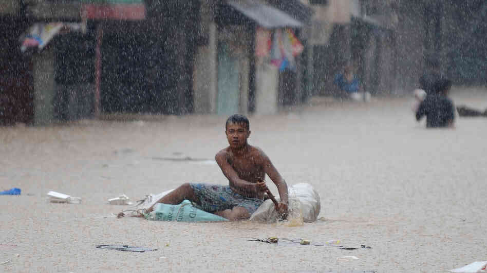 A man paddled an improvised raft along a flooded street in suburban Manila earlier today.