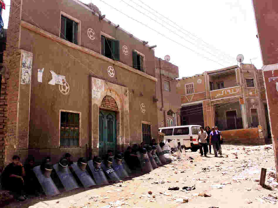 Egyptian riot police sit in the shade by damaged buildings as people walk through debris from the aftermath of clashes on Aug. 1 between Christians and Muslims in Dahshour, on the outskirts of Cairo. The violence was sparked by a dispute between a Muslim and Christian over laundered clothing.