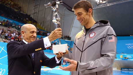 Michael Phelps accepts a trophy commemorating his status as the most-decorated Olympian from FINA president Julio Maglione. Phelps is retiring from Olympic swimming at 27.