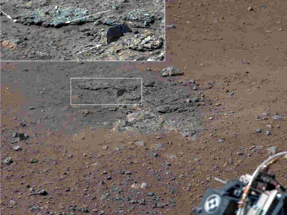 With the loose debris blasted away by the rockets, details of the underlying materials are clearly seen. Shown in the inset in the figure are pebbles up to 1.25 inches across (upper two arrows) and a larger clast 4 inches long protruding up by about 2 inches from the layer in which it is embedded. With the loose debris blasted away by the rockets, details of the underlying materials are clearly seen. Shown in the inset in the figure are pebbles up to 1.25 inches across (upper two arrows) and a larger clast 4 inches long protruding up by about 2 inches from the layer in which it is embedded.