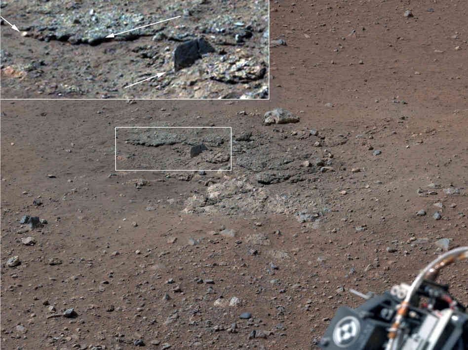 With the loose debris blasted away by the rockets, details of the underlying materials are clearly seen. Shown in the inset in the figure are pebbles up to 1.25 inches across (upper two arrows) and a larger clast 4 inches long protruding up by about 2 inches from the layer in which it is embedded. With the loose debris blasted away by the rockets, details of the underlying materials are clearly seen. Shown in the inset in the figure are pebbles up to 1.25 inches across (upper two arrows) and a larger clast 4 inches long protruding up by about 2 inches from the layer in which it is embedded.