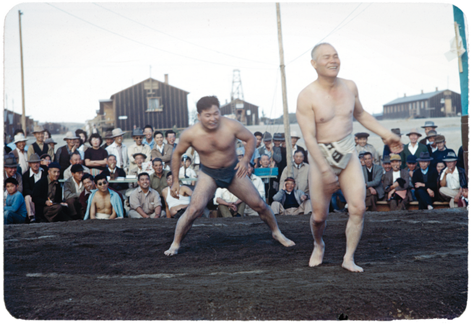 Sumo wrestlers share a light moment during a match in front of spectators.