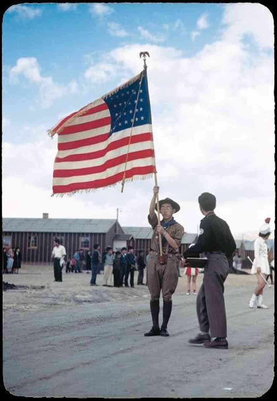A Boy Scout carrying an American flag leads a parade through the Heart Mountain camp.