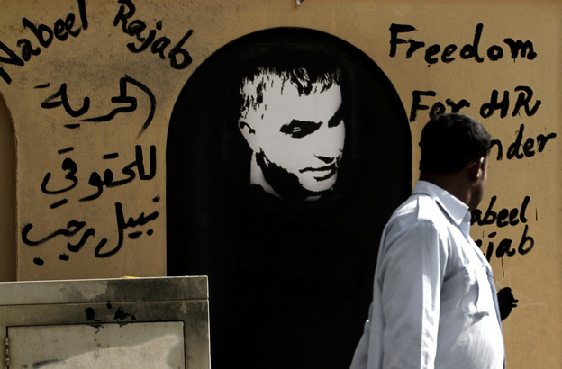 A man walks past a picture of human rights defender Nabeel Rajab and Arabic that reads, "freedom to human rights defender Nabeel Rajab."