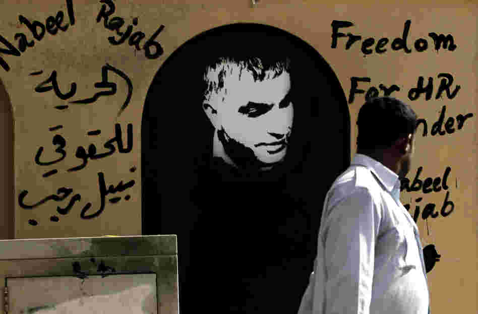 A man walks past a picture of human rights defender Nabeel Rajab and Arabic that reads, "freedom to human rights defender Nabeel Rajab."