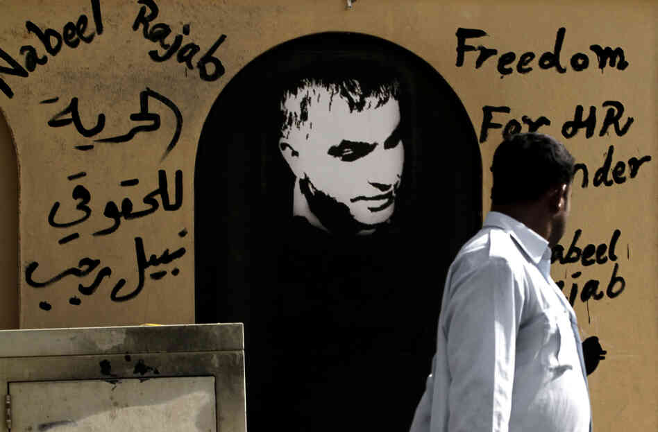 A man walks past a picture of human rights defender Nabeel Rajab and Arabic that reads, "freedom to human rights defender Nabeel Rajab."