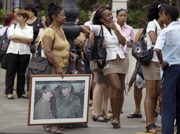 People, one holding an image of Cuba's President Raul Castro  and his brother Fidel Castro, wait in line at a bus stop in Havana last month.