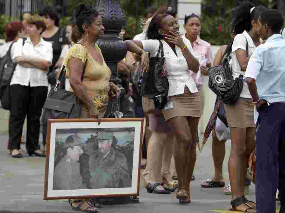 People, one holding an image of Cuba's President Raul Castro  and his brother Fidel Castro, wait in line at a bus stop in Havana last month.