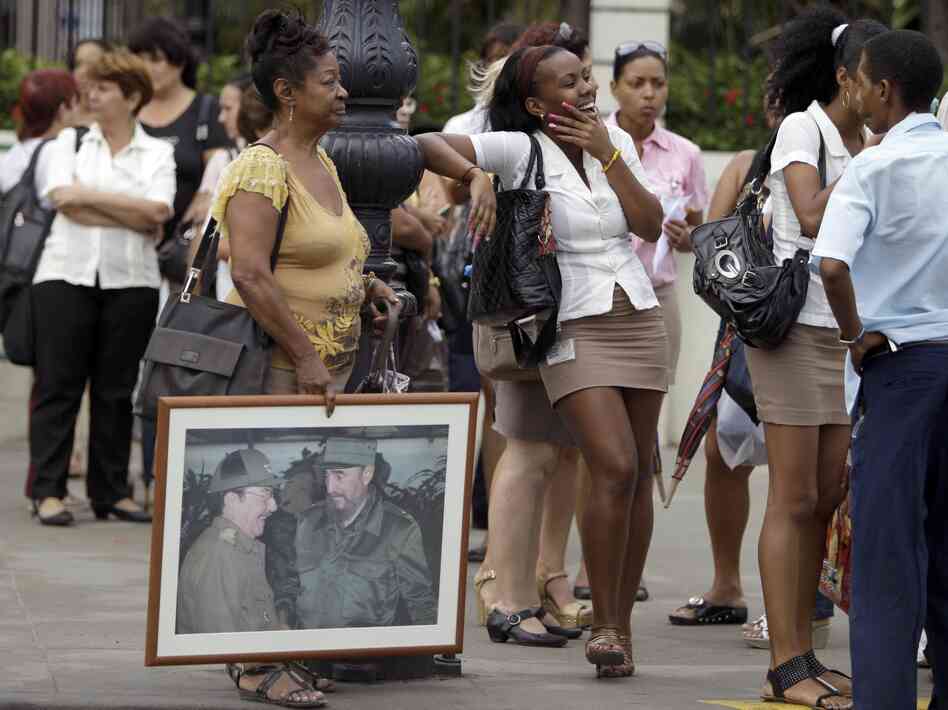 People, one holding an image of Cuba's President Raul Castro  and his brother Fidel Castro, wait in line at a bus stop in Havana last month.