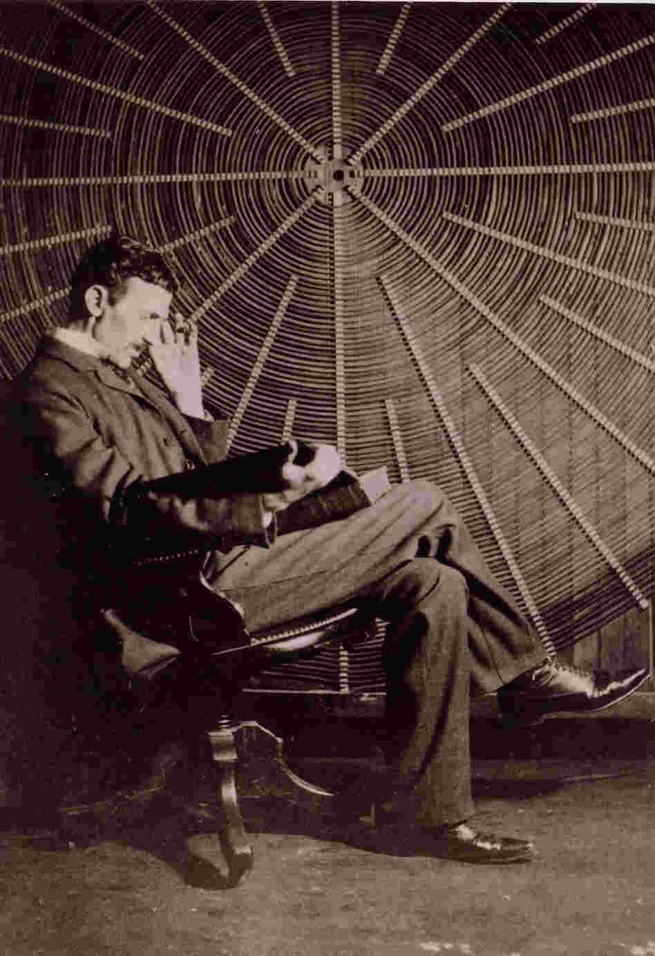 Tesla reads in front of the spiral coil of his high-frequency transformer at his lab on Houston Street in New York.