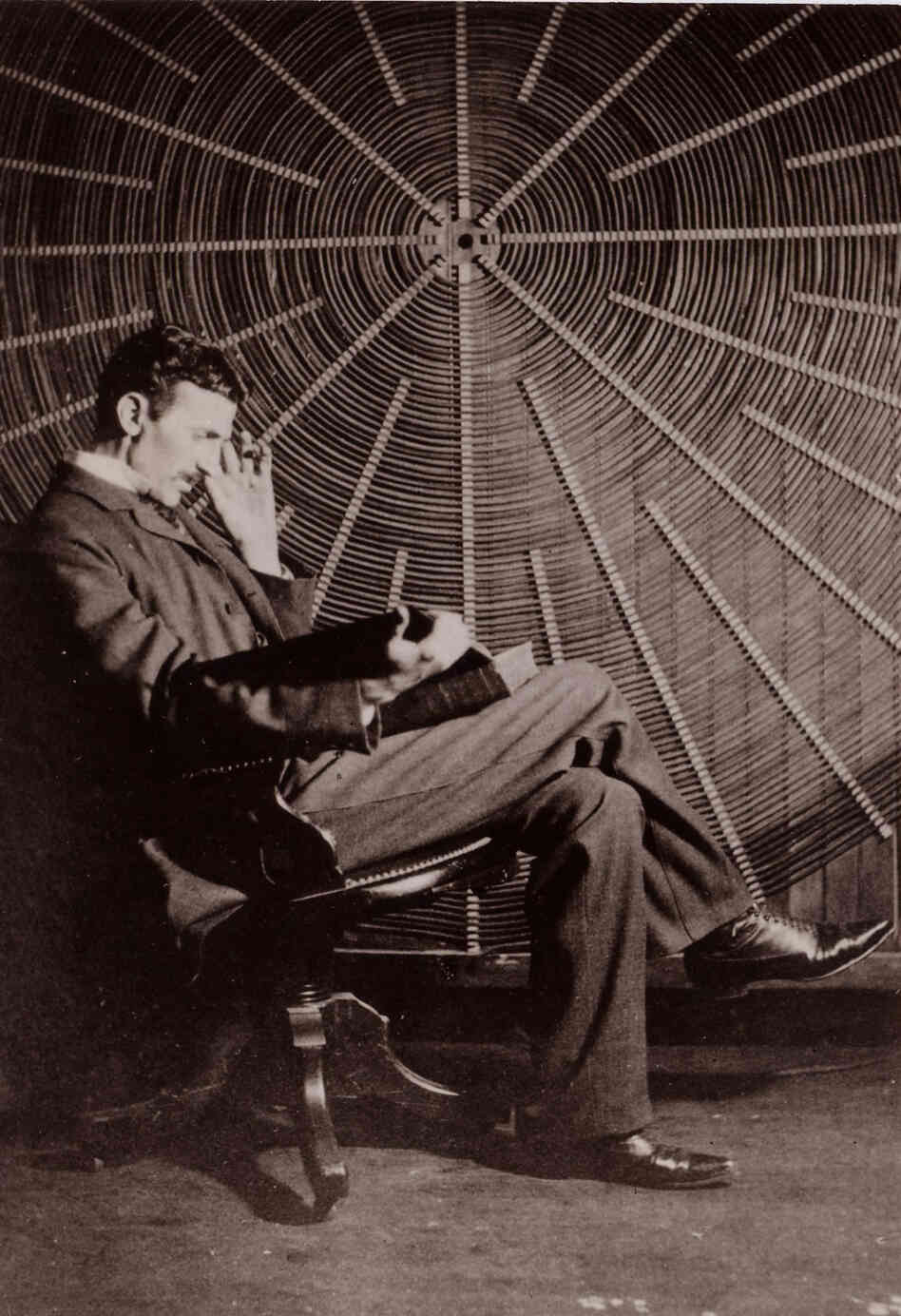 Tesla reads in front of the spiral coil of his high-frequency transformer at his lab on Houston Street in New York.
