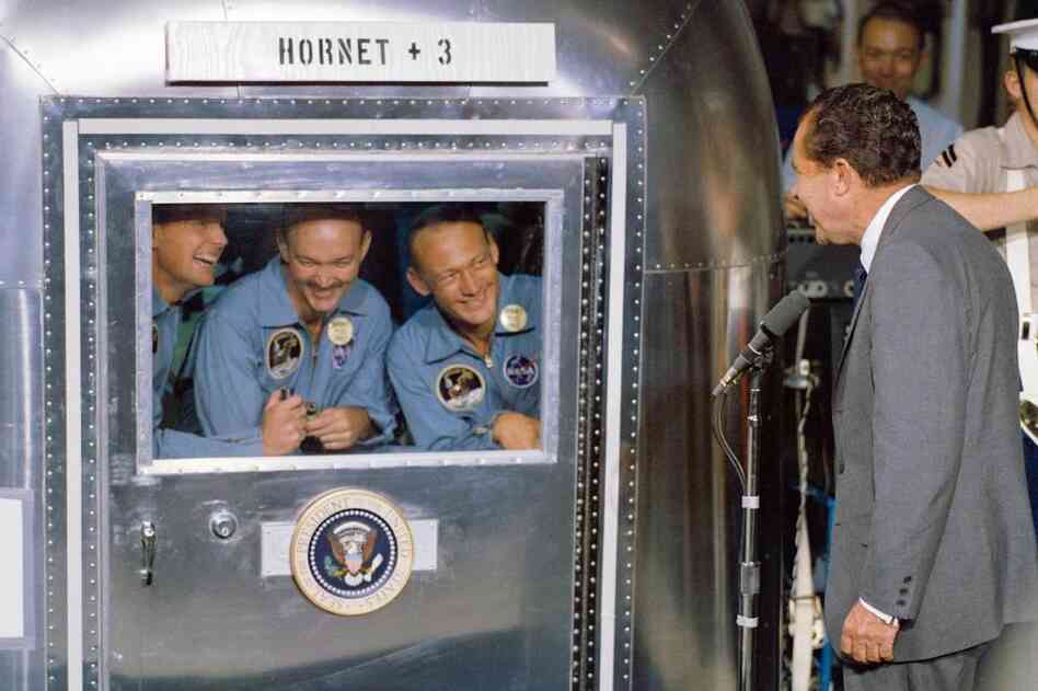 President Richard Nixon welcomes the Apollo 11 astronauts aboard the USS Hornet, prime recovery ship for the lunar landing mission. Armstrong (left) and his fellow colleagues are in the mobile quarantine facility.