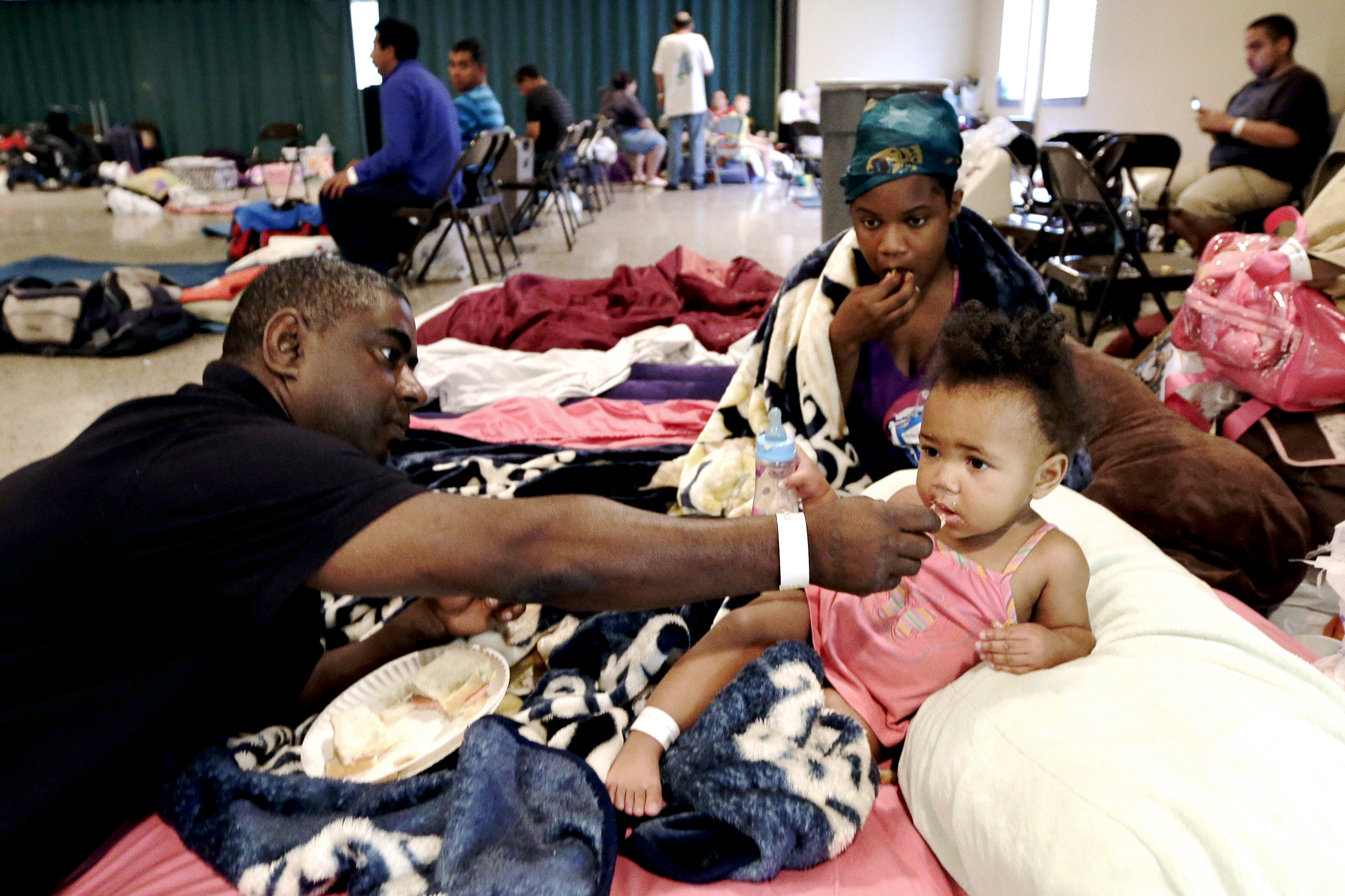 Gus Williams feeds his step-granddaughter, Somaya Washington, as her mother, Areonisha Washington, watches. They evacuated to a shelter in Houma, La.